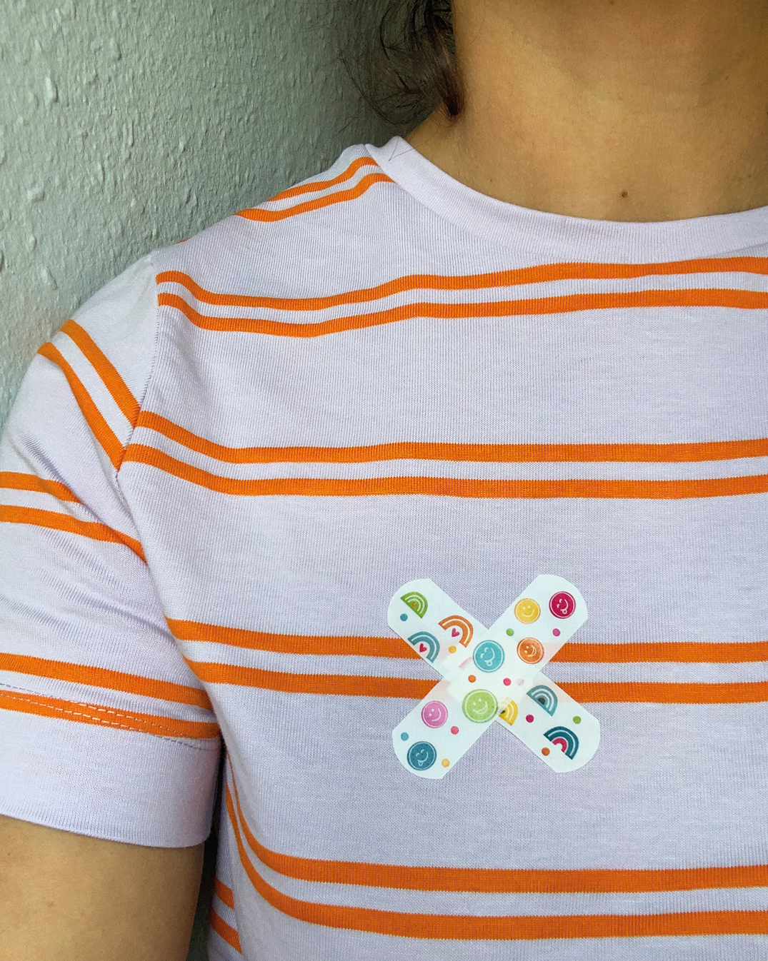 Kind mit zwei gekreuzten Pflastern auf das T-Shirt geklebt - Symbol für den Tag der pflegendne Eltern